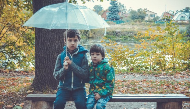 Children in the rain at autumn, holding an umbrella