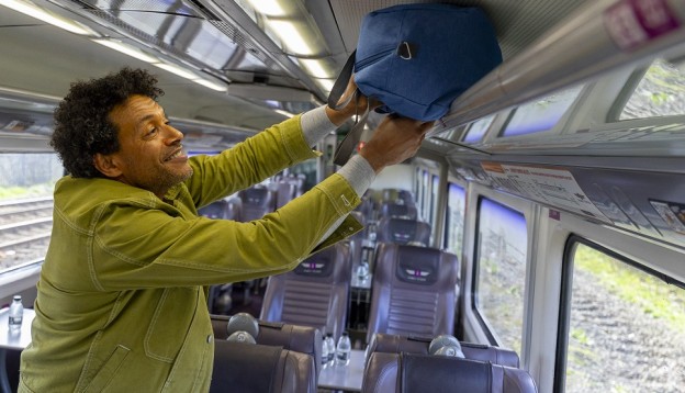 man putting bag in over-head storage on a train