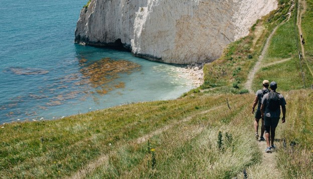 A man hiking on a grassy cliff near the sea. 